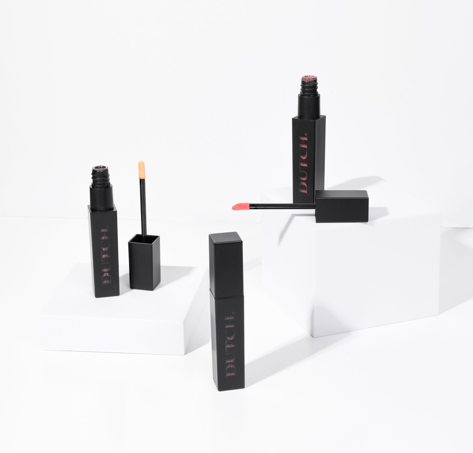 Three tubes of lipgloss in different colors. The tubes are matte black with DUTCH. transparant shown in it. De lipgloss colors are called Hope (transparant), High (bronze) and Hype (coral).